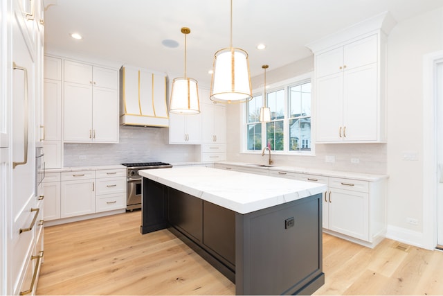 kitchen featuring premium range hood, light hardwood / wood-style flooring, high end stove, a kitchen island, and white cabinetry