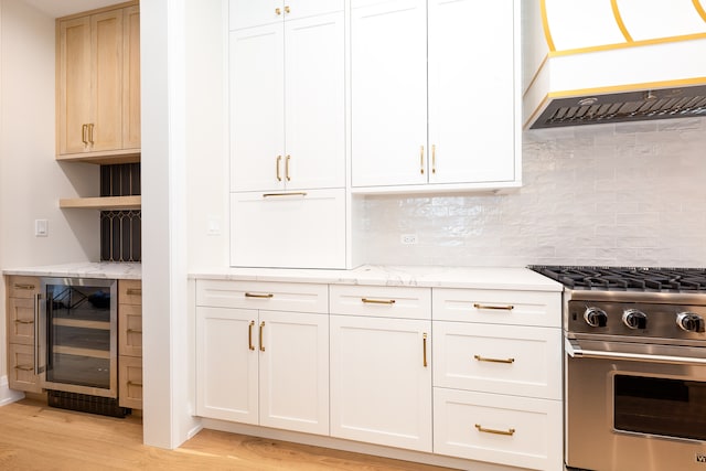 kitchen with backsplash, white cabinets, stainless steel stove, light hardwood / wood-style floors, and beverage cooler