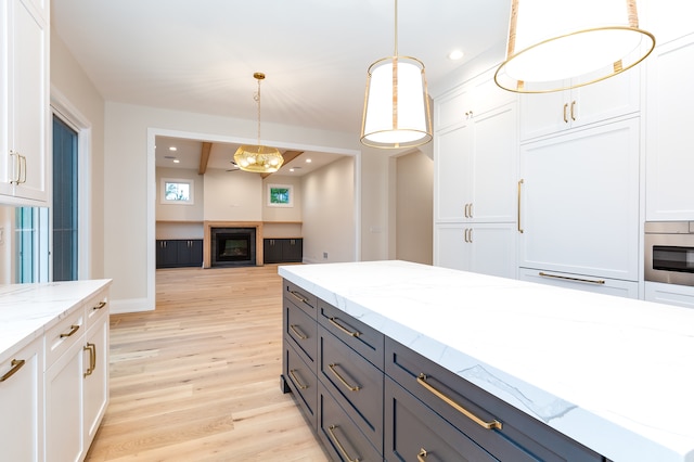 kitchen with light stone countertops, vaulted ceiling, pendant lighting, white cabinets, and light hardwood / wood-style floors