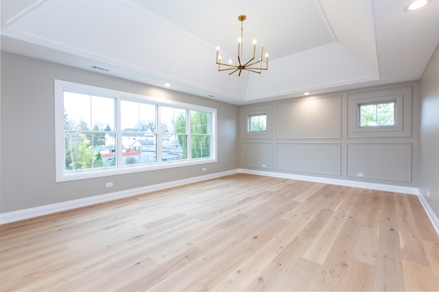 unfurnished room featuring a notable chandelier, a raised ceiling, and light wood-type flooring