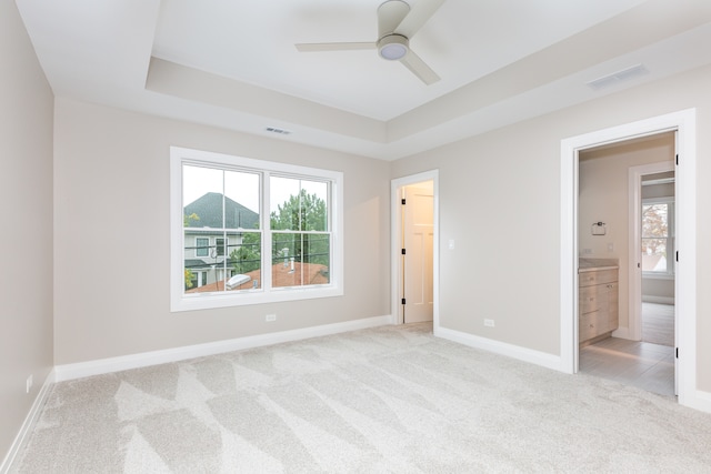 unfurnished bedroom featuring ceiling fan, a raised ceiling, light carpet, and ensuite bath