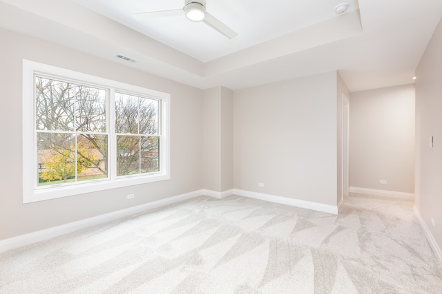 empty room featuring ceiling fan, light colored carpet, and a tray ceiling