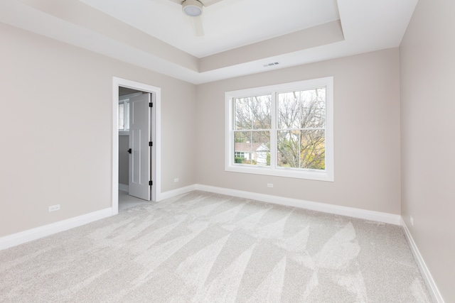 spare room featuring light carpet, a tray ceiling, and ceiling fan