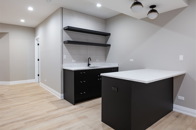 kitchen with kitchen peninsula, light wood-type flooring, sink, and backsplash