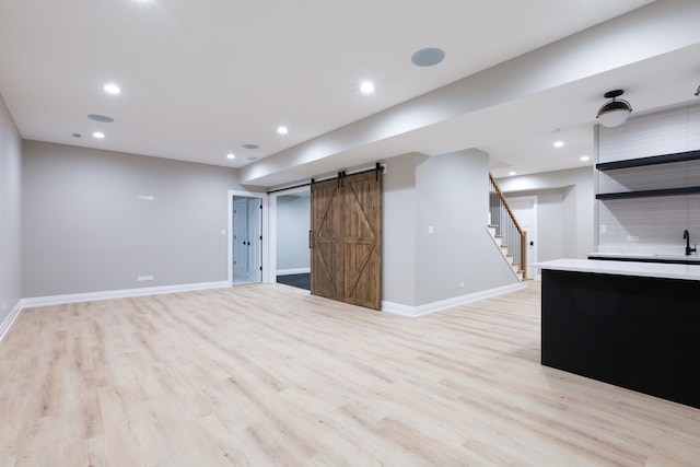 basement featuring a barn door, sink, and light hardwood / wood-style floors