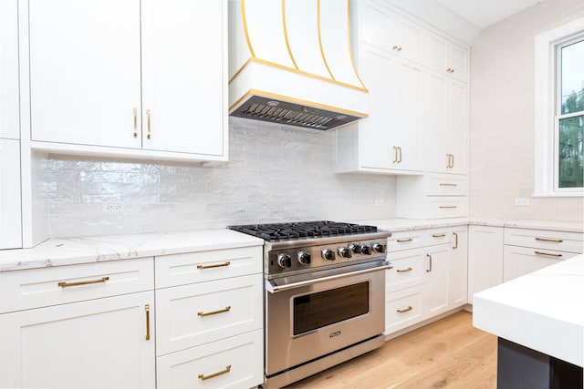 kitchen featuring backsplash, custom exhaust hood, luxury stove, light hardwood / wood-style flooring, and white cabinetry