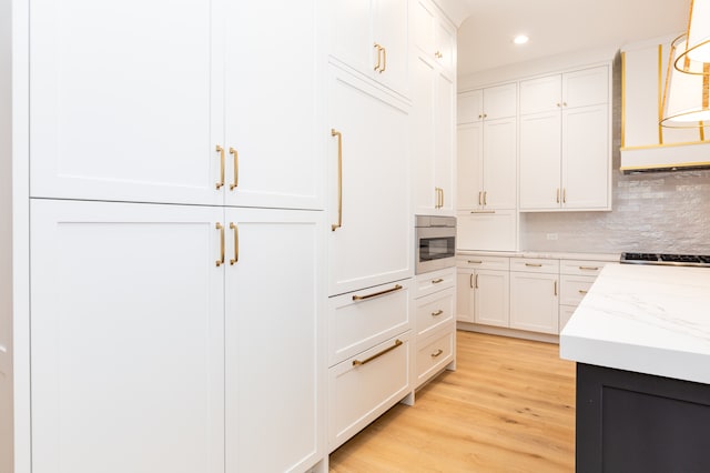 kitchen with exhaust hood, decorative backsplash, light wood-type flooring, decorative light fixtures, and white cabinetry