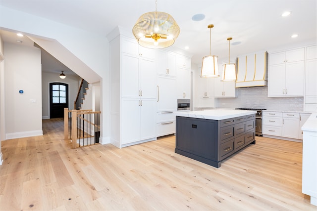 kitchen featuring white cabinetry, hanging light fixtures, stainless steel appliances, light hardwood / wood-style flooring, and premium range hood