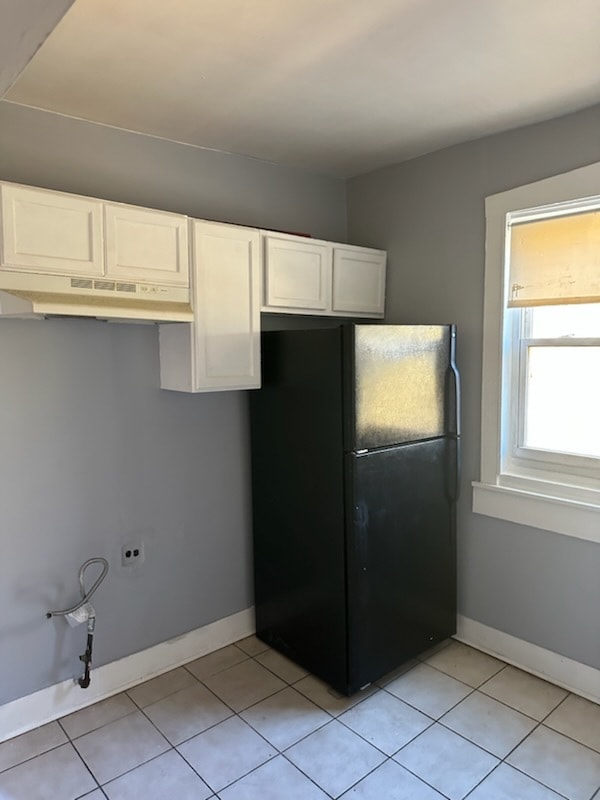 kitchen with white cabinetry, black fridge, and light tile patterned floors