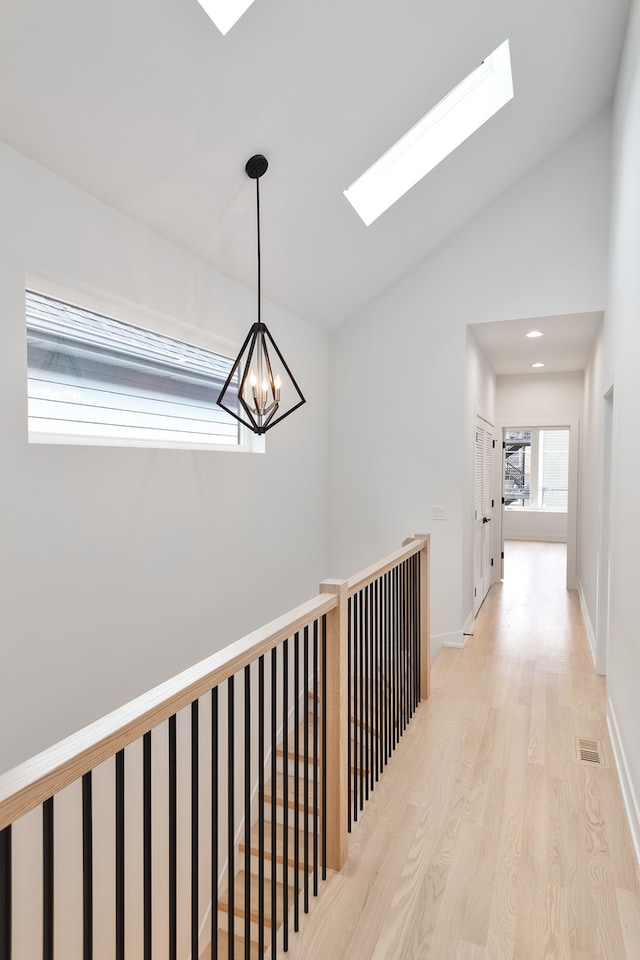 hallway featuring light wood-type flooring, an inviting chandelier, and lofted ceiling with skylight