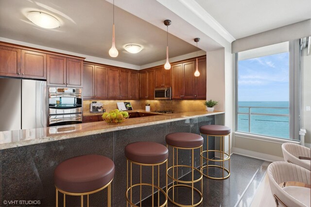 kitchen with light stone countertops, hanging light fixtures, tasteful backsplash, a water view, and appliances with stainless steel finishes