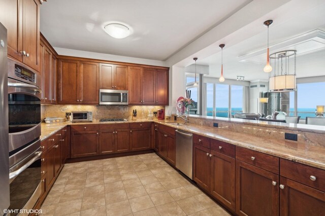 kitchen featuring light stone countertops, appliances with stainless steel finishes, backsplash, pendant lighting, and a water view