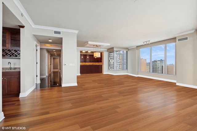 unfurnished living room with bar area, crown molding, and light wood-type flooring