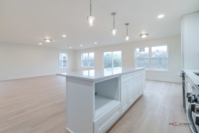 kitchen featuring a center island, white cabinets, light hardwood / wood-style flooring, stainless steel range, and decorative light fixtures