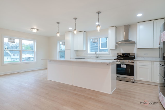 kitchen with white cabinetry, stainless steel range, wall chimney range hood, and light hardwood / wood-style flooring