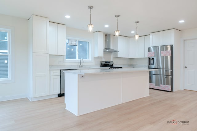 kitchen with white cabinets, wall chimney range hood, decorative light fixtures, a kitchen island, and stainless steel appliances