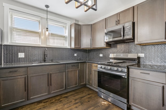 kitchen with sink, pendant lighting, decorative backsplash, appliances with stainless steel finishes, and dark wood-type flooring