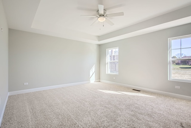 carpeted empty room featuring a raised ceiling, ceiling fan, and a healthy amount of sunlight