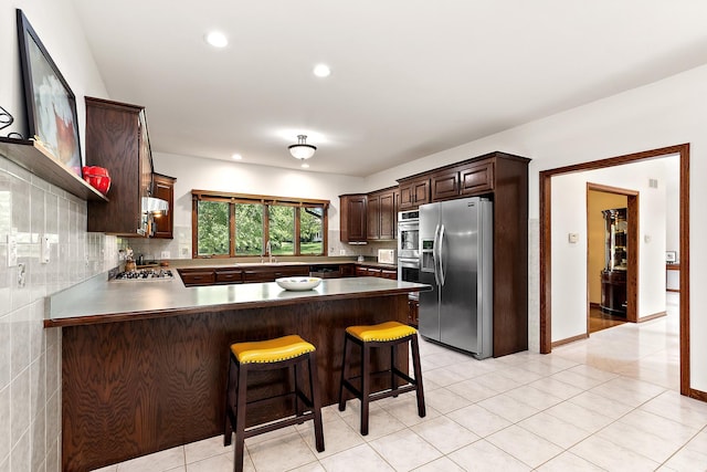 kitchen featuring sink, appliances with stainless steel finishes, backsplash, a kitchen bar, and kitchen peninsula