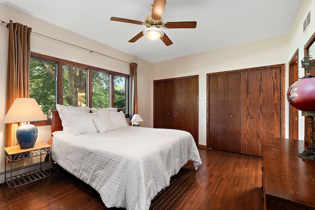 bedroom featuring ceiling fan, two closets, dark wood-type flooring, and a baseboard radiator