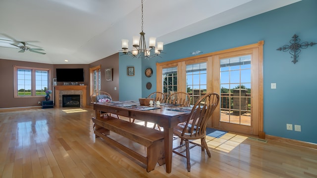 dining space featuring a tile fireplace, light wood-type flooring, and ceiling fan with notable chandelier