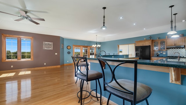 kitchen featuring pendant lighting, black fridge with ice dispenser, ceiling fan with notable chandelier, backsplash, and light wood-type flooring