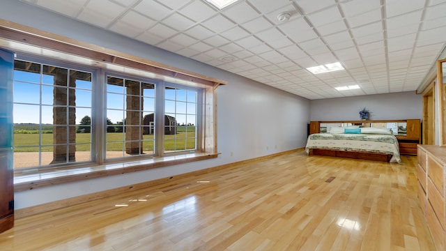 unfurnished bedroom with multiple windows, a drop ceiling, and light hardwood / wood-style floors