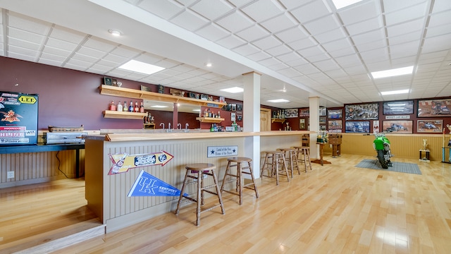 bar featuring light wood-type flooring and a drop ceiling