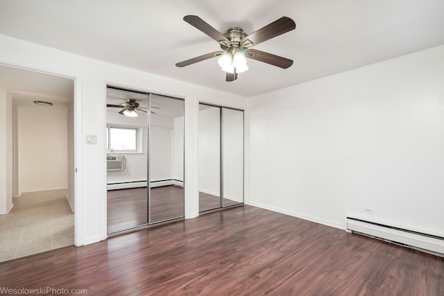 unfurnished bedroom with ceiling fan, dark hardwood / wood-style flooring, multiple closets, and a baseboard heating unit