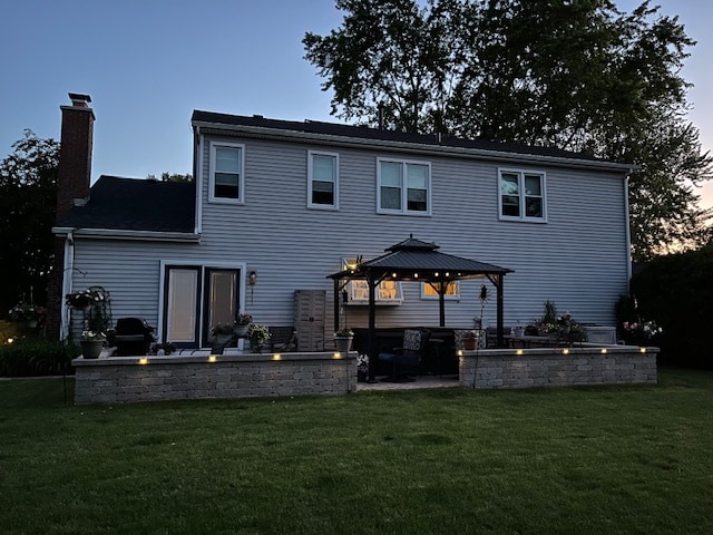 back house at dusk with a gazebo and a lawn