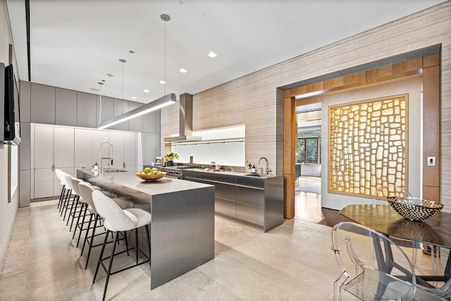 kitchen with pendant lighting, sink, wall chimney range hood, and a kitchen island with sink