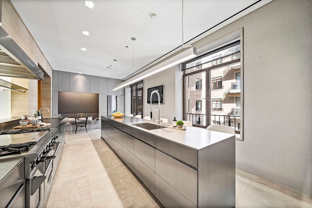 kitchen featuring sink, wall chimney range hood, high end stainless steel range oven, a spacious island, and decorative light fixtures