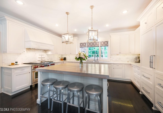 kitchen with a kitchen bar, custom range hood, a kitchen island, stainless steel stove, and white cabinetry