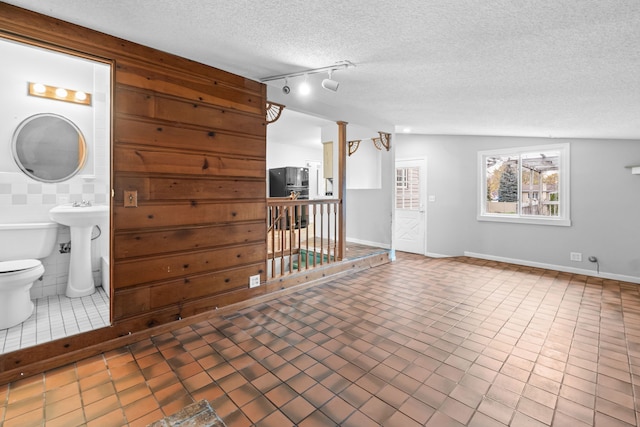 interior space featuring sink, tile patterned flooring, a textured ceiling, lofted ceiling, and tile walls