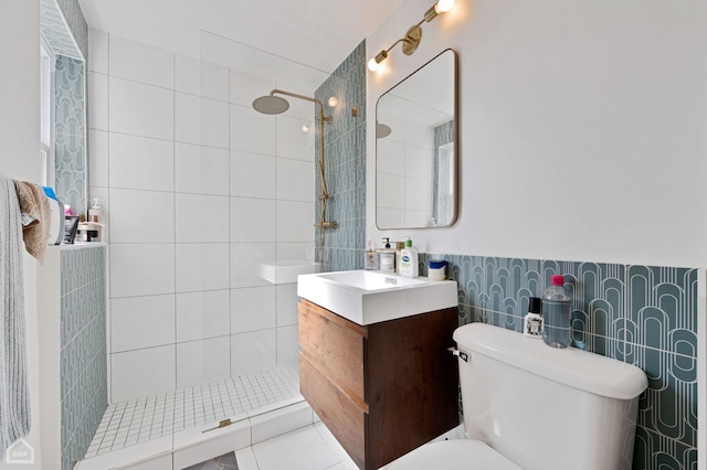 bathroom featuring tiled shower, toilet, tile walls, vanity, and tile patterned flooring