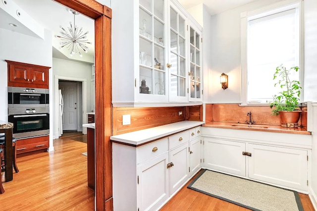 kitchen featuring pendant lighting, sink, white cabinets, stainless steel double oven, and light hardwood / wood-style flooring