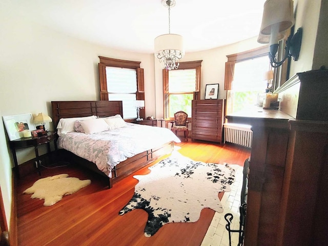 bedroom with an inviting chandelier, radiator heating unit, and light hardwood / wood-style floors