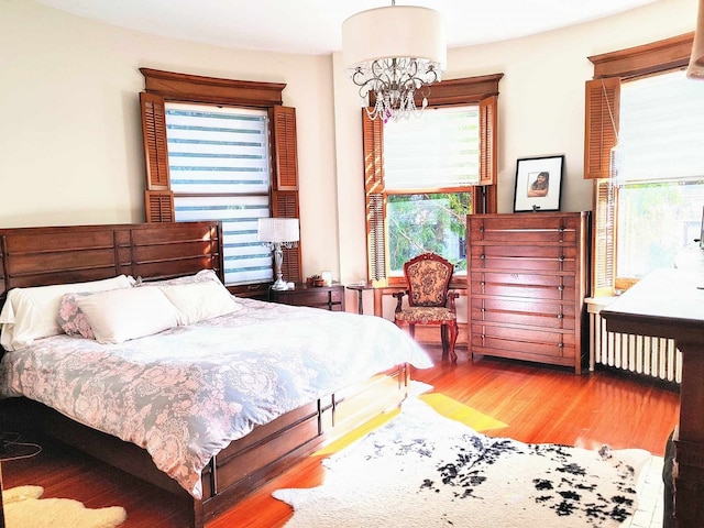 bedroom with multiple windows, wood-type flooring, radiator, and an inviting chandelier