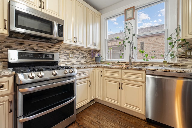 kitchen featuring light stone countertops, sink, dark wood-type flooring, stainless steel appliances, and cream cabinets