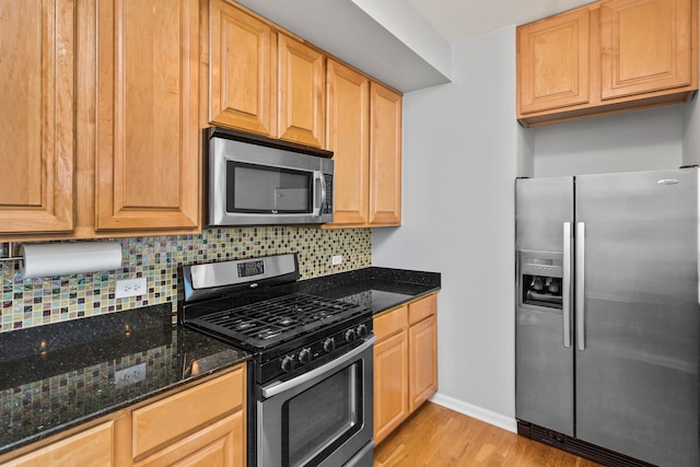 kitchen featuring decorative backsplash, stainless steel appliances, dark stone counters, and light hardwood / wood-style flooring