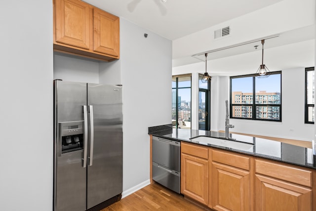 kitchen featuring sink, dark stone counters, pendant lighting, appliances with stainless steel finishes, and light wood-type flooring