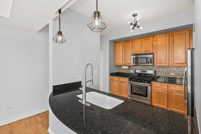 kitchen with decorative light fixtures, stainless steel appliances, dark stone countertops, and sink