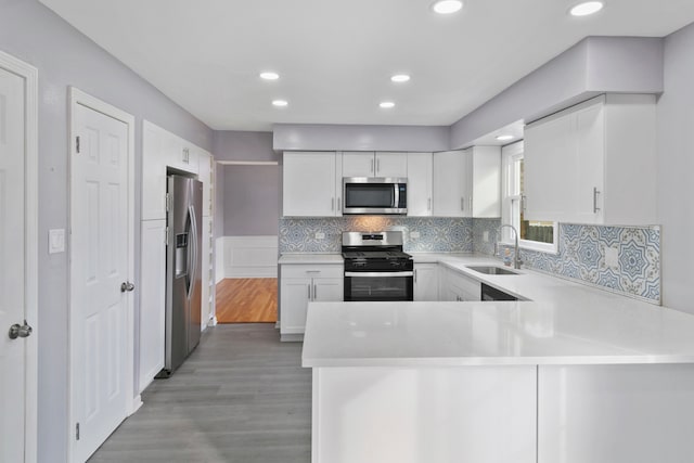 kitchen with white cabinetry, sink, kitchen peninsula, light hardwood / wood-style floors, and appliances with stainless steel finishes