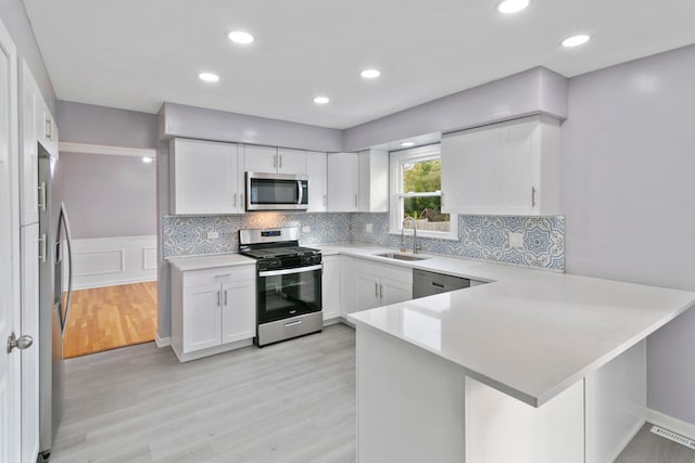 kitchen featuring white cabinetry, sink, light hardwood / wood-style flooring, kitchen peninsula, and appliances with stainless steel finishes