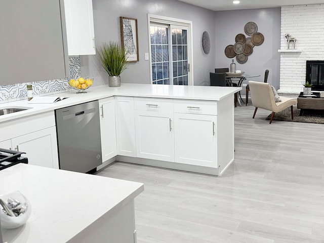 kitchen featuring dishwasher, kitchen peninsula, white cabinetry, and a fireplace