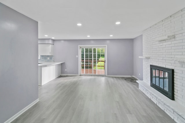 unfurnished living room featuring light wood-type flooring and a brick fireplace