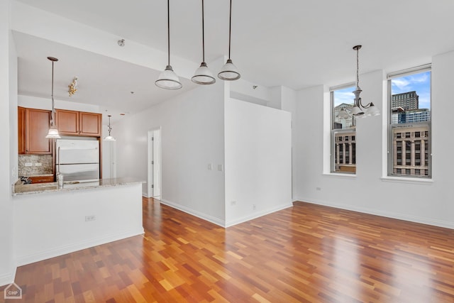 interior space with backsplash, light stone countertops, decorative light fixtures, white fridge, and wood-type flooring