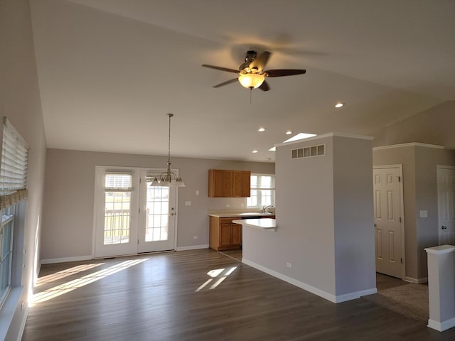 unfurnished living room with ceiling fan with notable chandelier, a healthy amount of sunlight, dark hardwood / wood-style floors, and vaulted ceiling