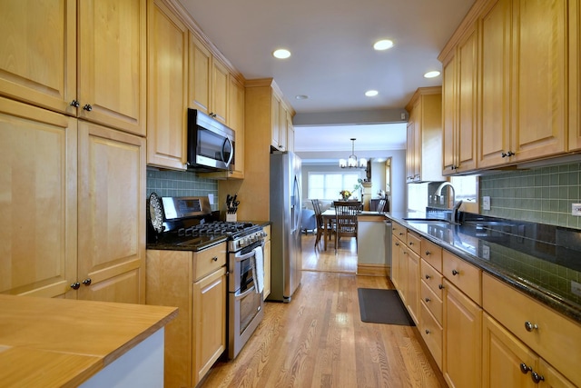 kitchen with sink, decorative backsplash, light wood-type flooring, appliances with stainless steel finishes, and decorative light fixtures