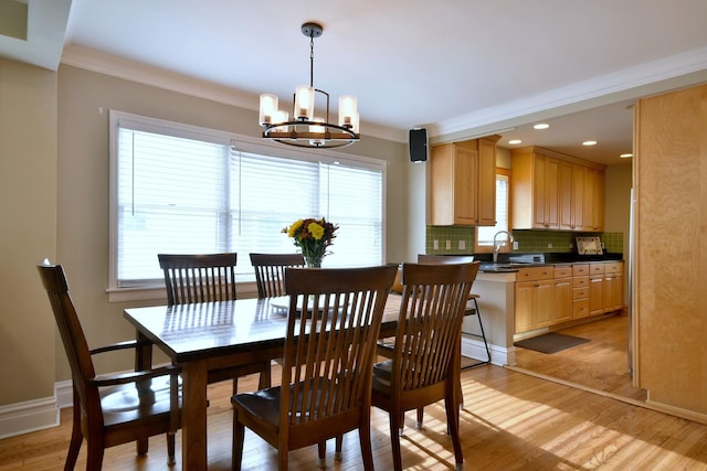 dining space with ornamental molding, light wood-type flooring, and a notable chandelier